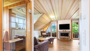 A spacious living area with a fireplace, wooden ceiling, and a large window. - Holiday Apartment 'Type B1, 50sqm' with Mountain View, Shared Terrace and Wi-Fi (Feldberg (Schwarzwald))