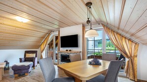 A dining area with a wooden table, grey chairs, a television mounted on the wall, and a fireplace. - Holiday Apartment 'Type B1, 50sqm' with Mountain View, Shared Terrace and Wi-Fi (Feldberg (Schwarzwald))
