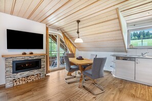 A modern kitchen with a built-in stove, a dining area with a table and chairs, a TV mounted on the wall, and a window with a view of greenery. - Holiday Apartment 'Type B1, 50sqm' with Mountain View, Shared Terrace and Wi-Fi (Feldberg (Schwarzwald))