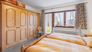 A bedroom with two beds, a wooden wardrobe, a chair, and a window with curtains.