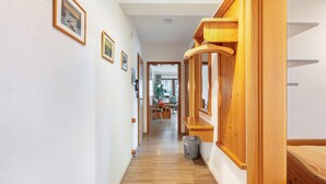 A hallway with wooden flooring, framed pictures on the walls, and a trash bin.