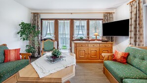 A living room with a sofa, a coffee table, a TV, and a window with curtains.