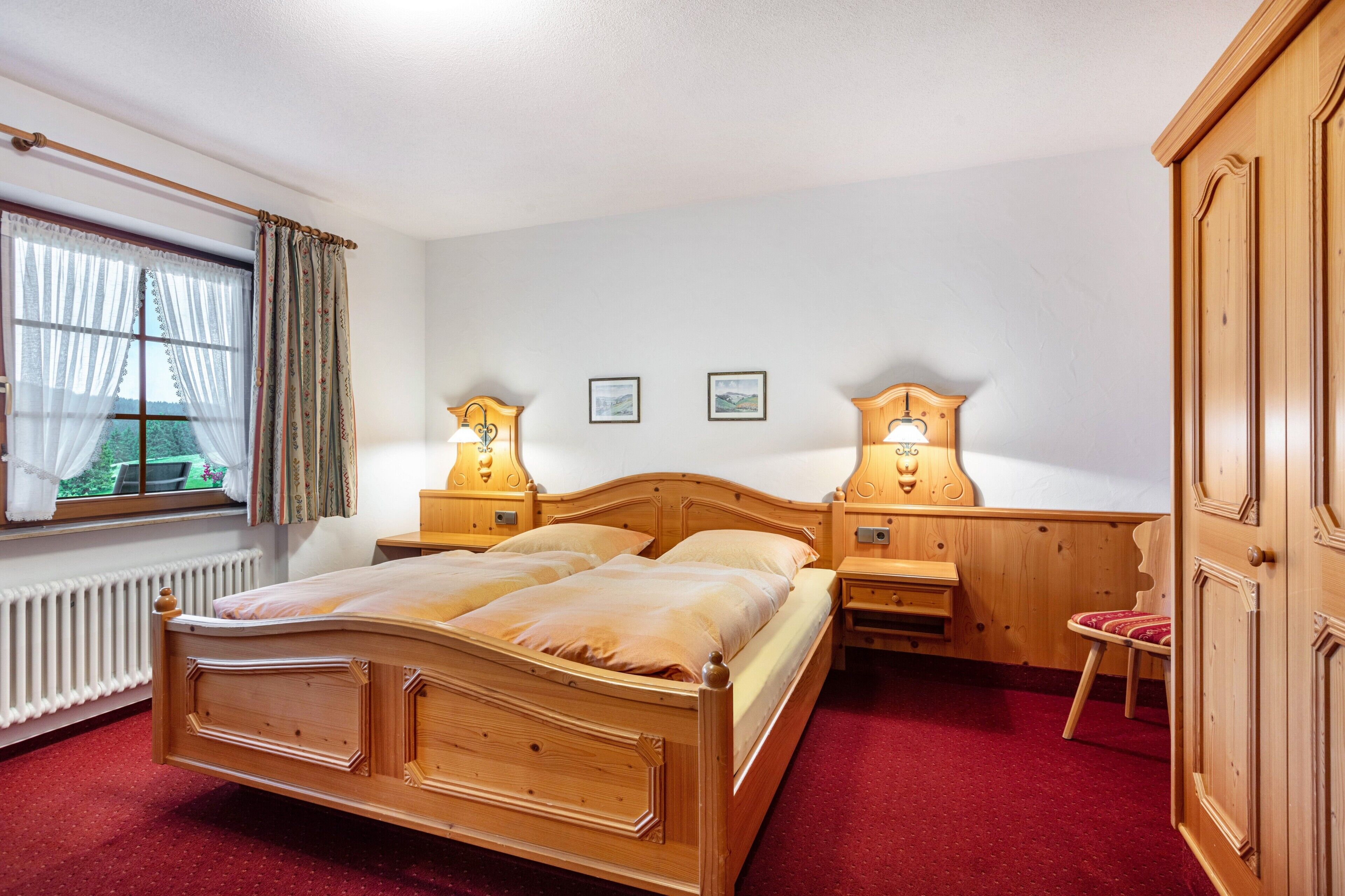 A wooden bed with two nightstands, a chair, and a wardrobe in a room with a red carpet.