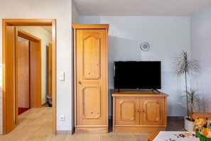 A room with a wooden wardrobe, a television on a wooden stand, a potted plant, and a red carpet.