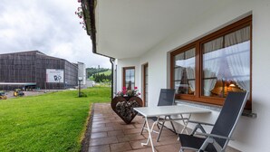 A patio with a table and chairs, a heart-shaped planter with flowers, and a view of a building in the background. - Holiday Apartment 'Type B Apartment 2' with Mountain View, Shared Terrace and Wi-Fi (Feldberg (Schwarzwald))