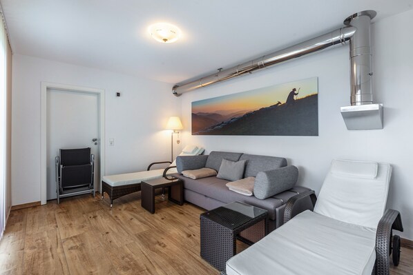 Une pièce comprenant un canapé, un fauteuil inclinable, une petite table, une lampe et un tableau accroché au mur.