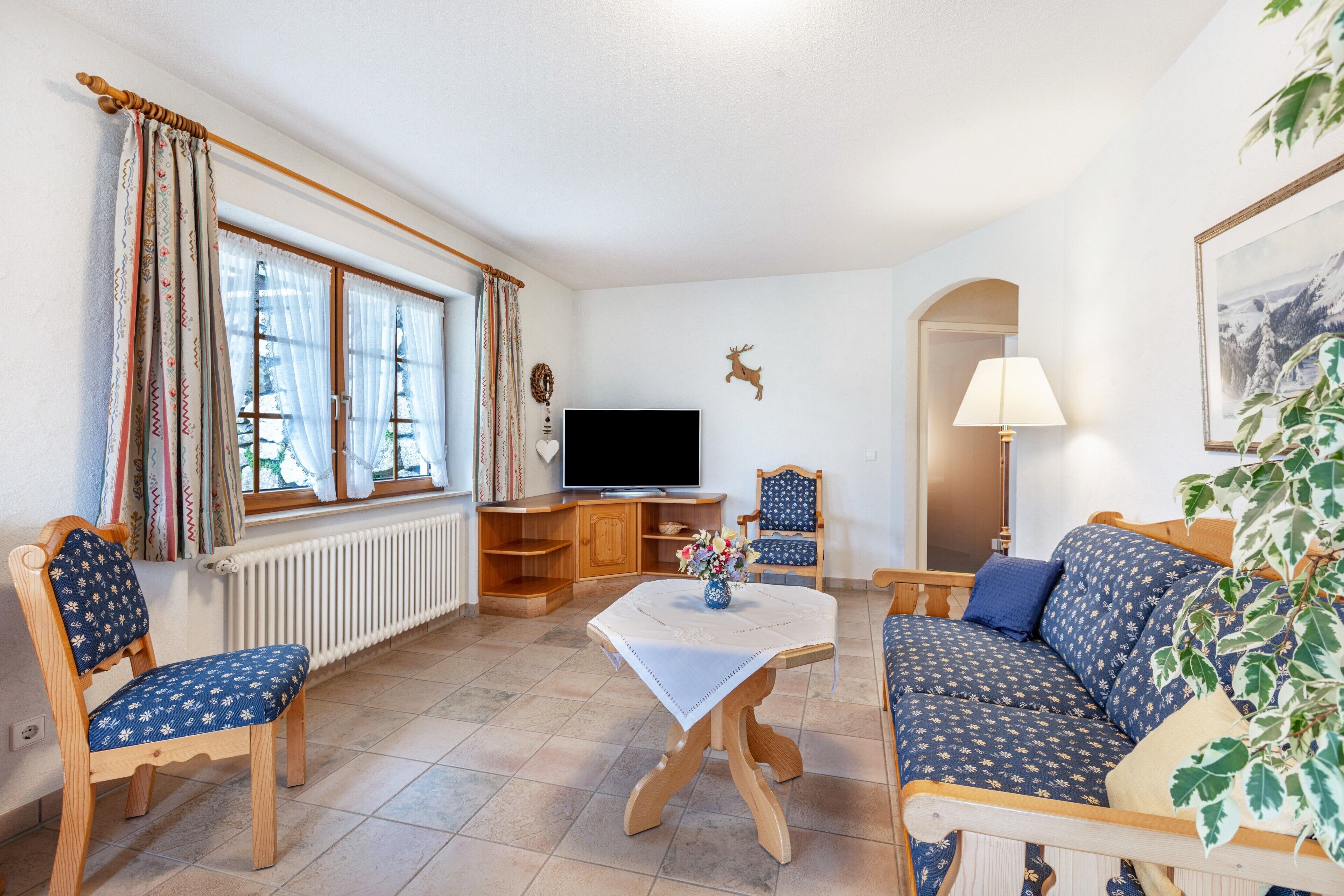 A living room with a sofa, chairs, a table, a television, and a plant.