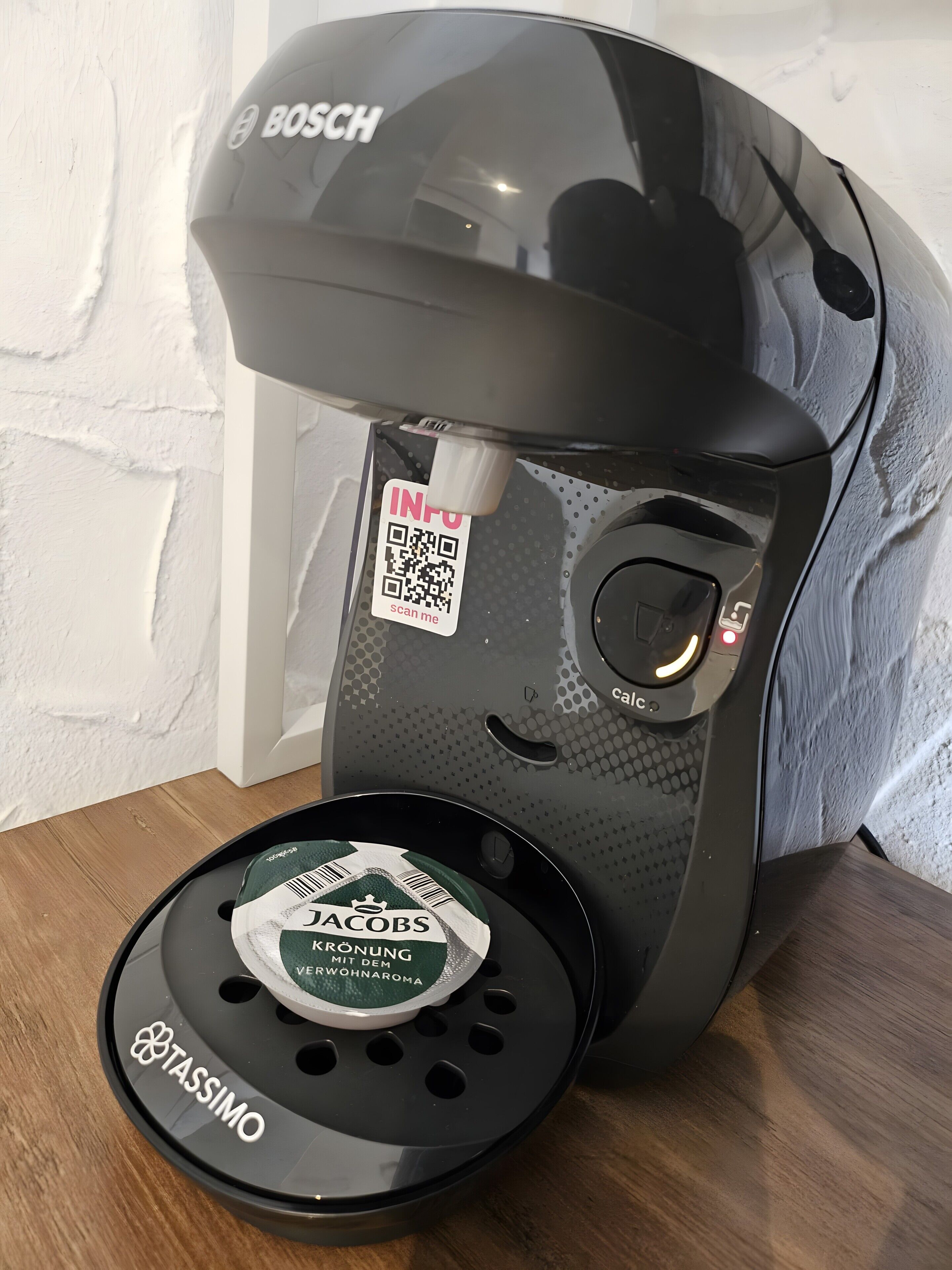 Una macchina per caffè con un codice QR e una cialda per caffè su un ripiano di legno.