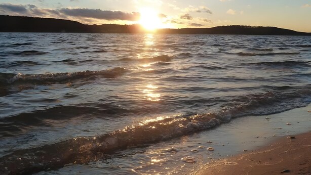 A beach with waves, a sunset, and a distant hill. - 'Im Gässla' Holiday Apartment with Wi-Fi (Spalt)