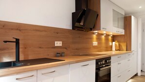 A modern kitchen with a wooden countertop, stainless steel sink, built-in oven, and white cabinetry. - 'Im Gässla' Holiday Apartment with Wi-Fi (Spalt)