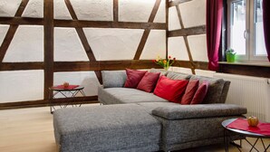 A room with a large grey sectional sofa, a small round table, and a window with curtains. - 'Im Gässla' Holiday Apartment with Wi-Fi (Spalt)