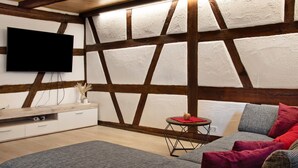 A modern room with exposed wooden beams, a flat-screen TV, a sofa, and a small table with a red mat. - 'Im Gässla' Holiday Apartment with Wi-Fi (Spalt)