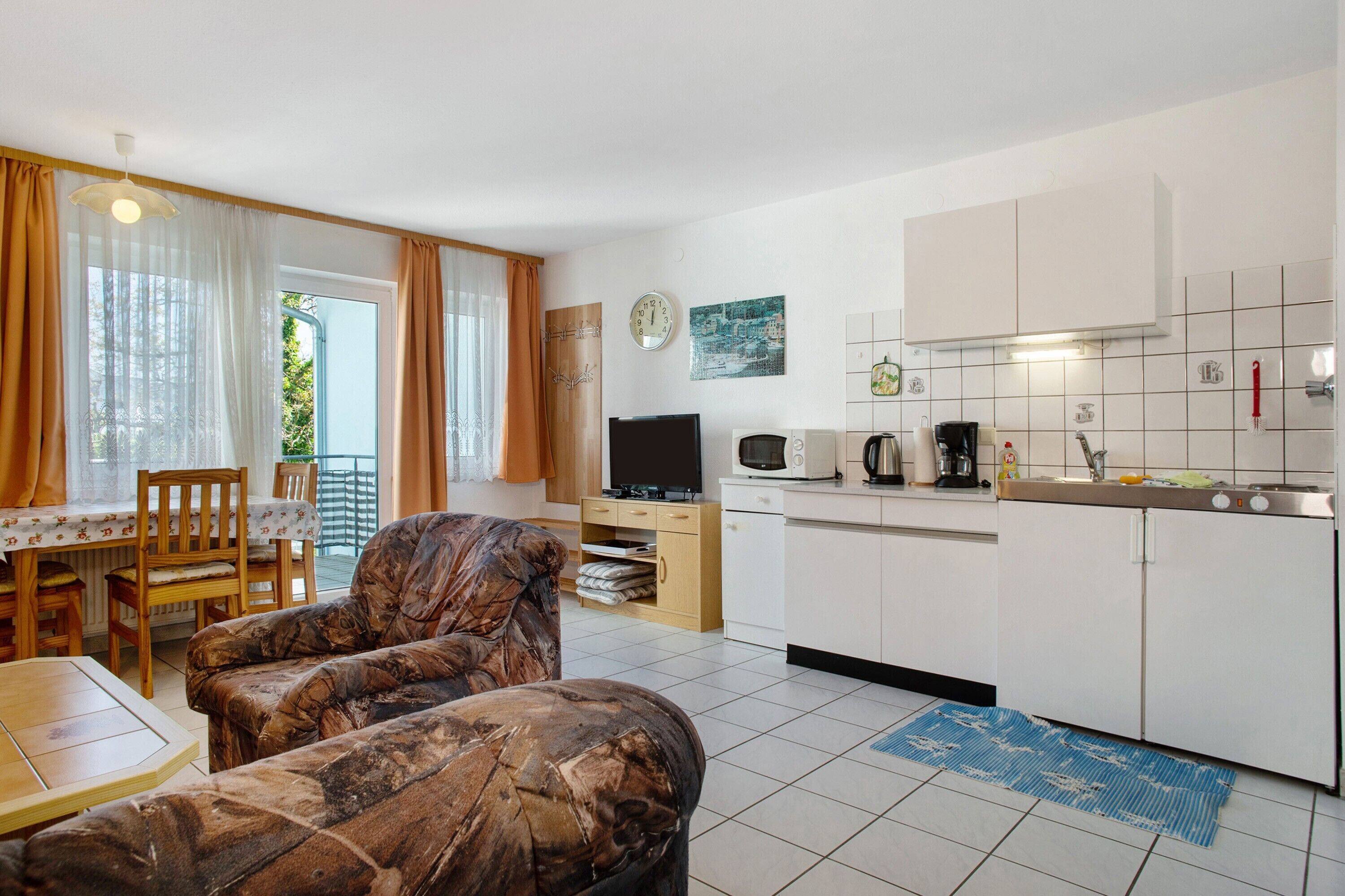Un espai habitable compacte amb zona de dinar, sofà, petita cuina i vista per la finestra.
