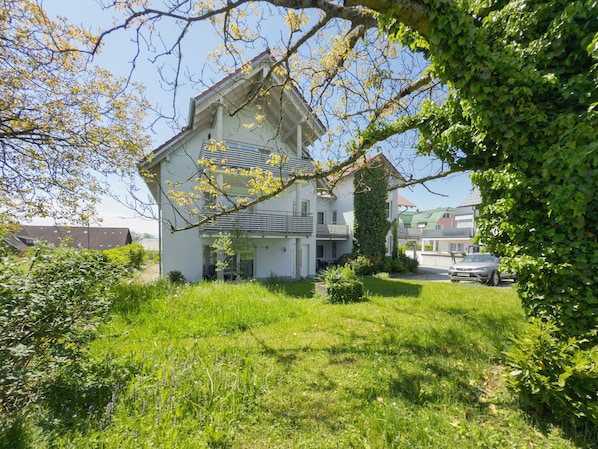 A two-story house with a balcony, surrounded by a well-maintained lawn and a tree.