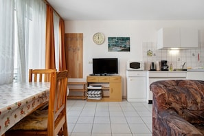 A compact living space with a dining table, a TV, a sofa, and a kitchen area.