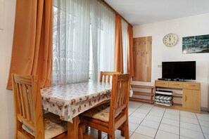 Uma sala de jantar com uma mesa, cadeiras, cortinas, uma televisão e um relógio na parede.