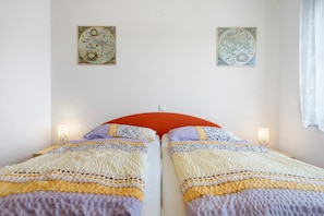 A double bed with a red headboard, two bedside tables with wall-mounted lamps, and two framed maps on the wall.