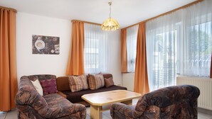 Ein Wohnzimmer mit einer Couch, zwei Sesseln, einem Couchtisch und einer Pendelleuchte.