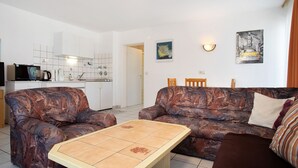 Ein Wohnzimmer mit einer Couch, einem Couchtisch, einer Küche im Hintergrund und einem Gemälde an der Wand.