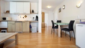 Una cocina moderna con armarios blancos, un comedor con mesa de vidrio y una sala de estar compacta.