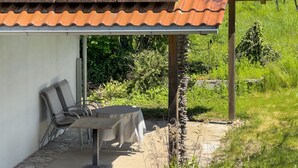 Un área de estar techada al aire libre con una mesa y sillas, un conjunto de paneles solares en el techo y un muro de piedra.