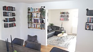 A modern living room with a dining area, featuring bookshelves, a sofa, a coffee table, and a small plant. - Holiday Home 'Hq16 - Modern' with Private Terrace, Balcony and Wi-Fi (Neuenburg am Rhein)