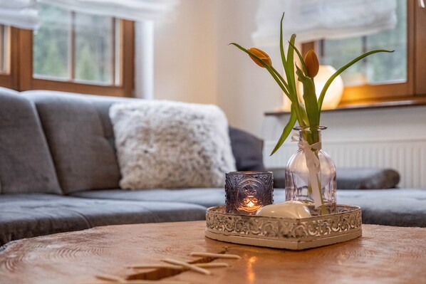 A cozy living room with a sofa, a decorative glass vase with flowers, and a candle on a wooden table.
