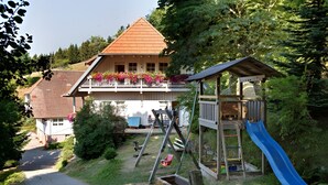 A house with a wooden deck, a blue slide, and a red swing set.