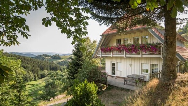 A two-story house with a balcony, surrounded by trees and a view of the countryside.