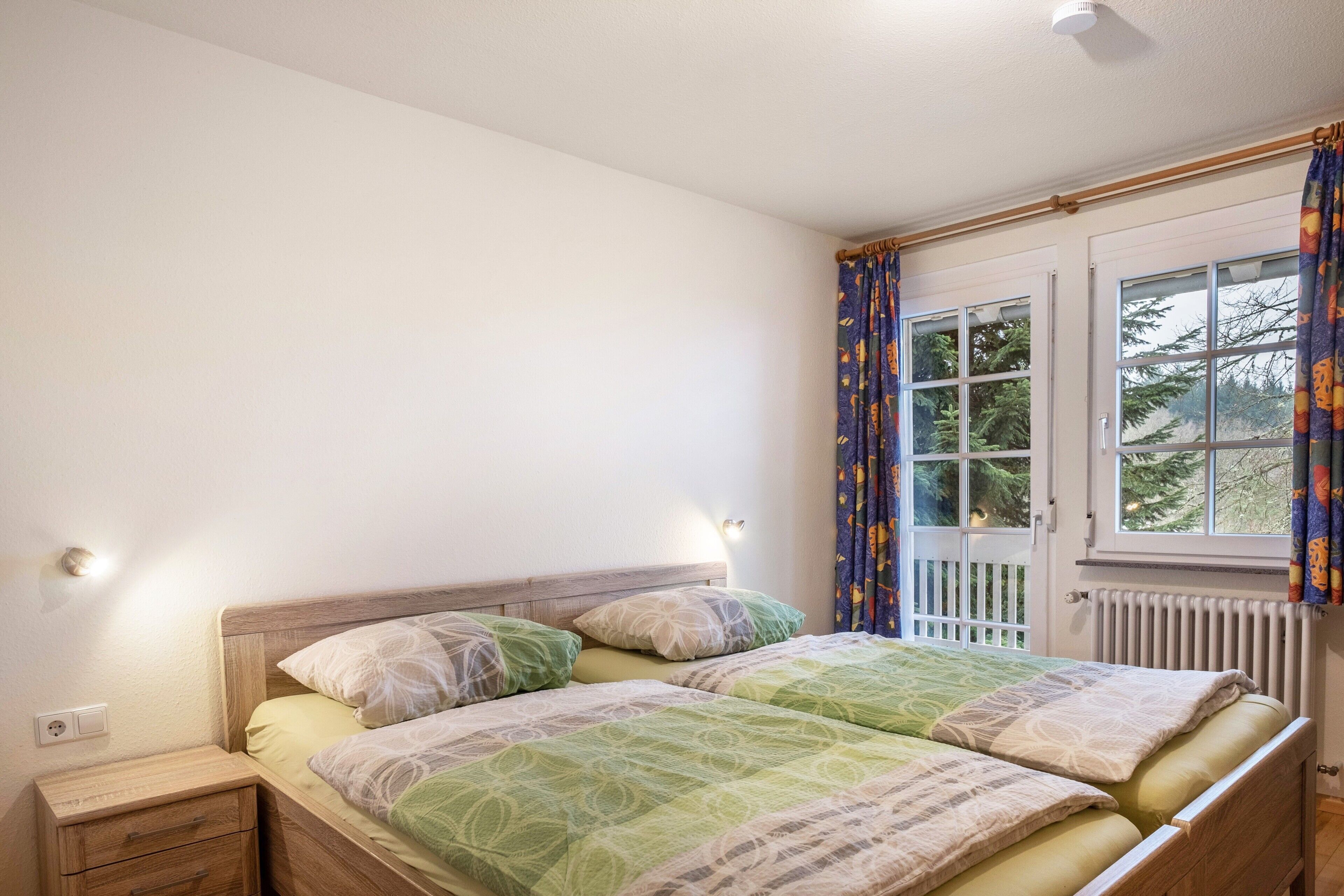 Un dormitorio con cama, mesitas de noche, una ventana con cortinas y un radiador.
