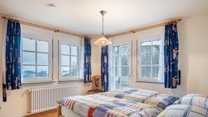 A bedroom with two beds, large windows, a radiator, and a hanging light fixture.