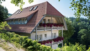 A two-story house with a steeply pitched roof, dormer windows, and a balcony with flower boxes.