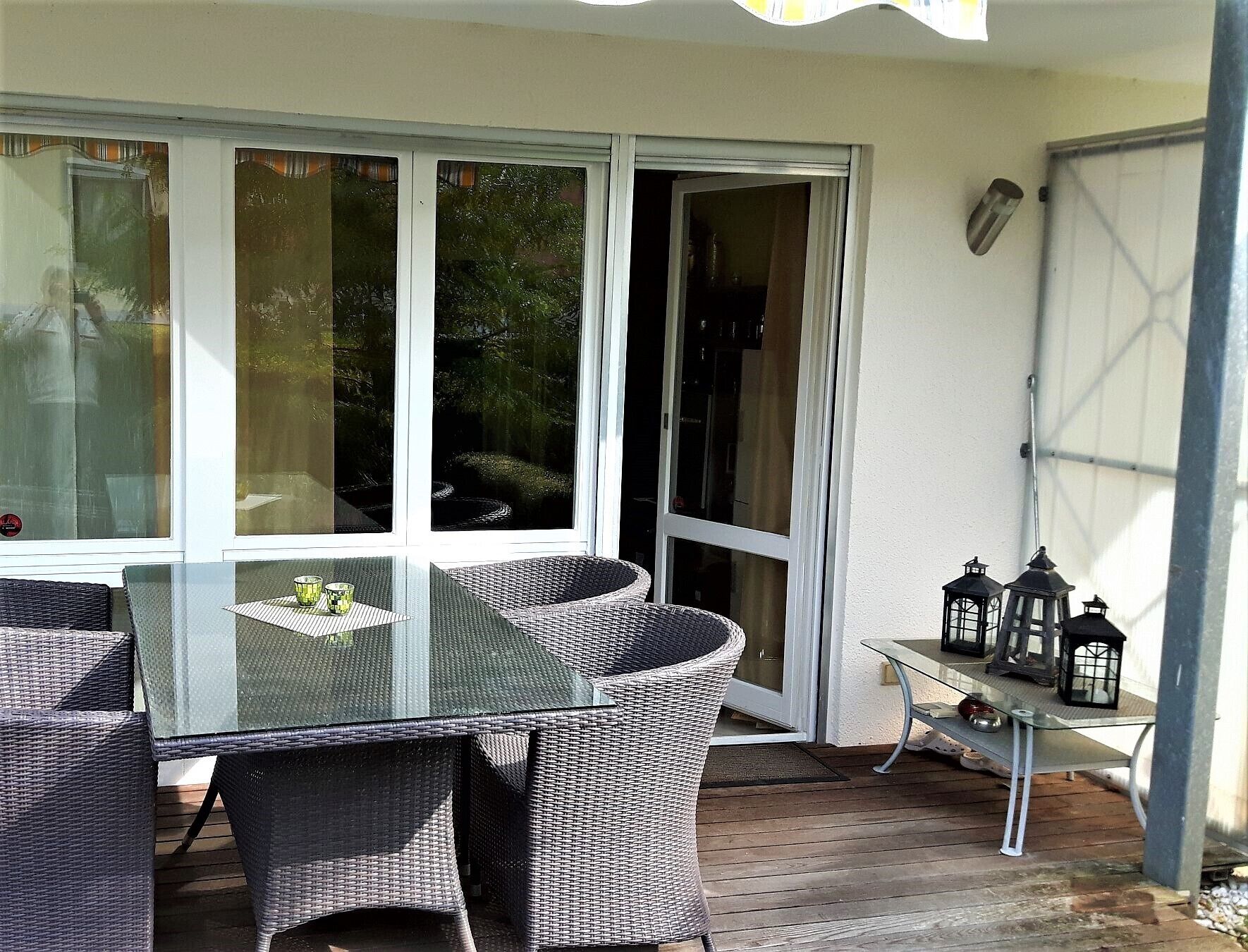 Een terras met rieten meubilair, een glazen tafel en een schuifpui.
