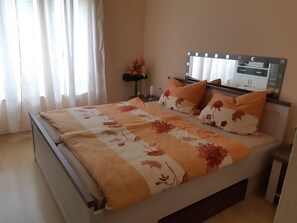 Ein Schlafzimmer mit einem Bett, einem Nachttisch, einem Spiegel und einem Fenster mit Vorhängen.