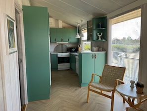 A compact kitchen with teal cabinets, a white stove, and a dining area with a wooden chair and table.