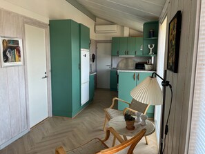 A compact kitchen with teal cabinets, a white refrigerator, and a dining area with wooden chairs and a small table. - Lovely summer house 50 meters from the beach (Glesborg)