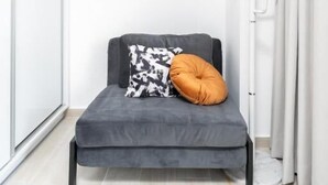 Una habitación pequeña y moderna con un sofá cama gris, un cojín estampado y un cojín naranja decorativo.