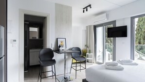 Una habitación de hotel moderna con una cama grande, un escritorio con dos sillas, un televisor y un balcón con vistas a árboles.