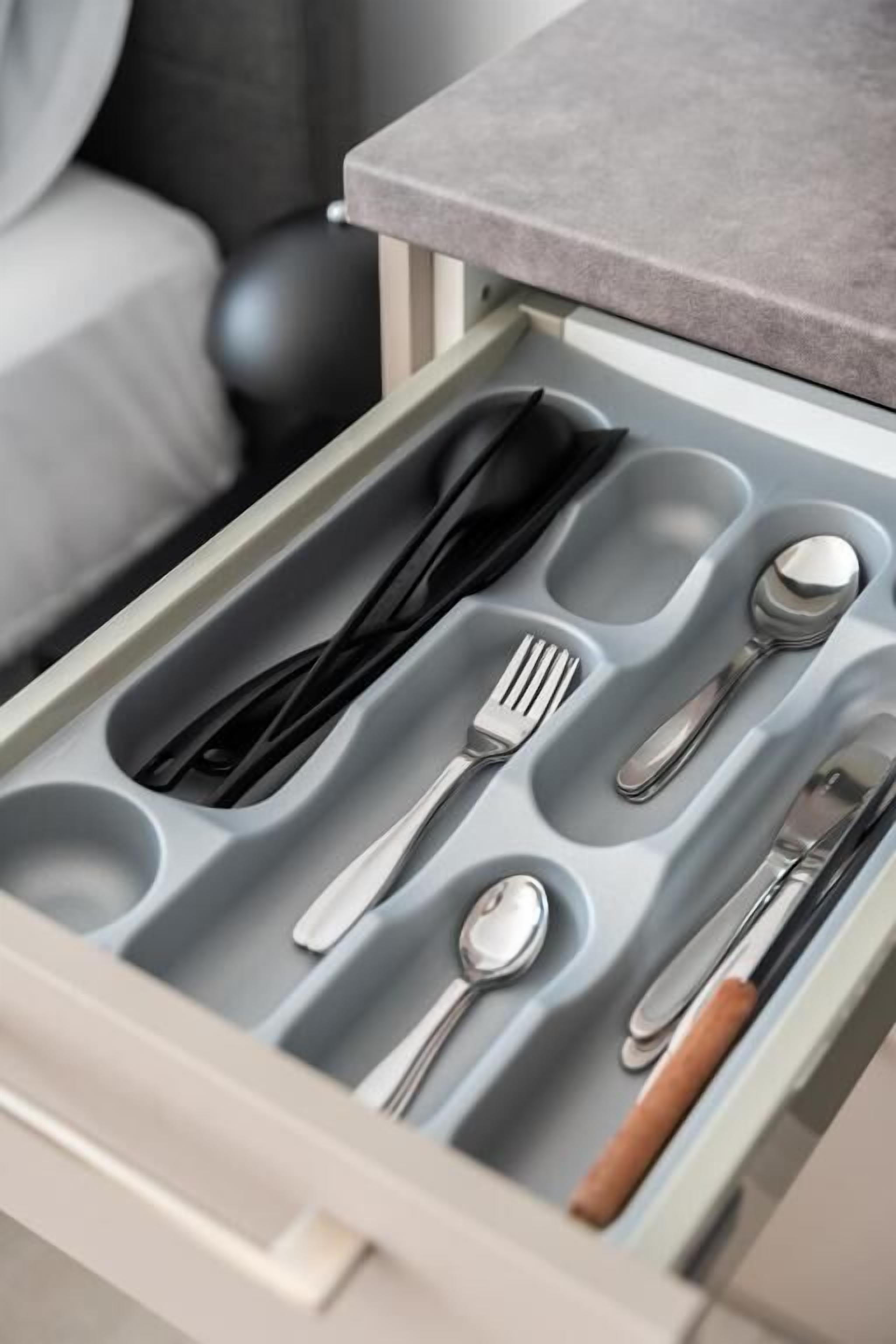 A drawer with compartments containing cutlery and a spoon.