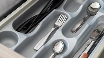 A drawer with compartments containing cutlery and a spoon.