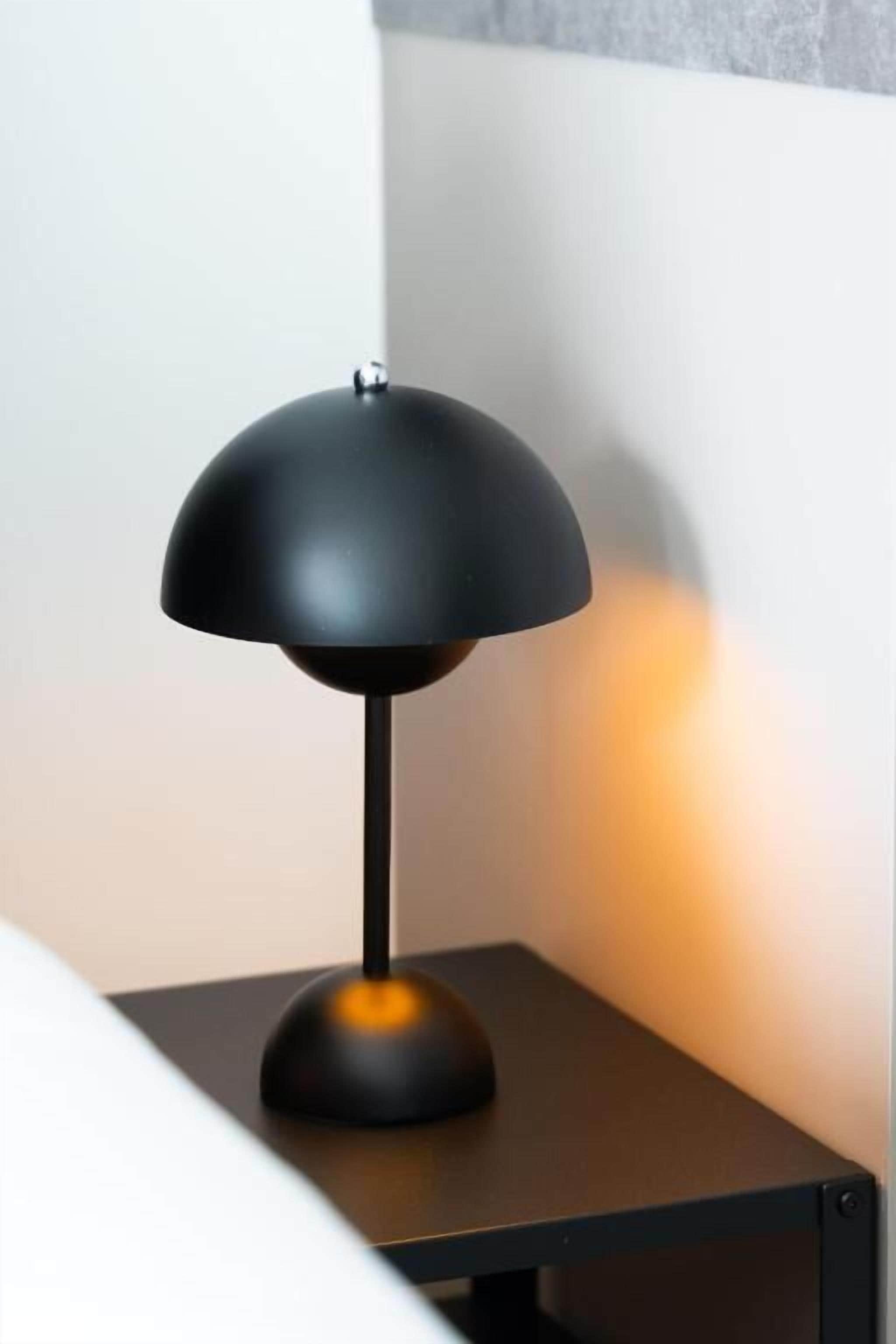 Una lampada da tavolo nera con paralume a cupola su un tavolo nero, su fondo di parete bianca.