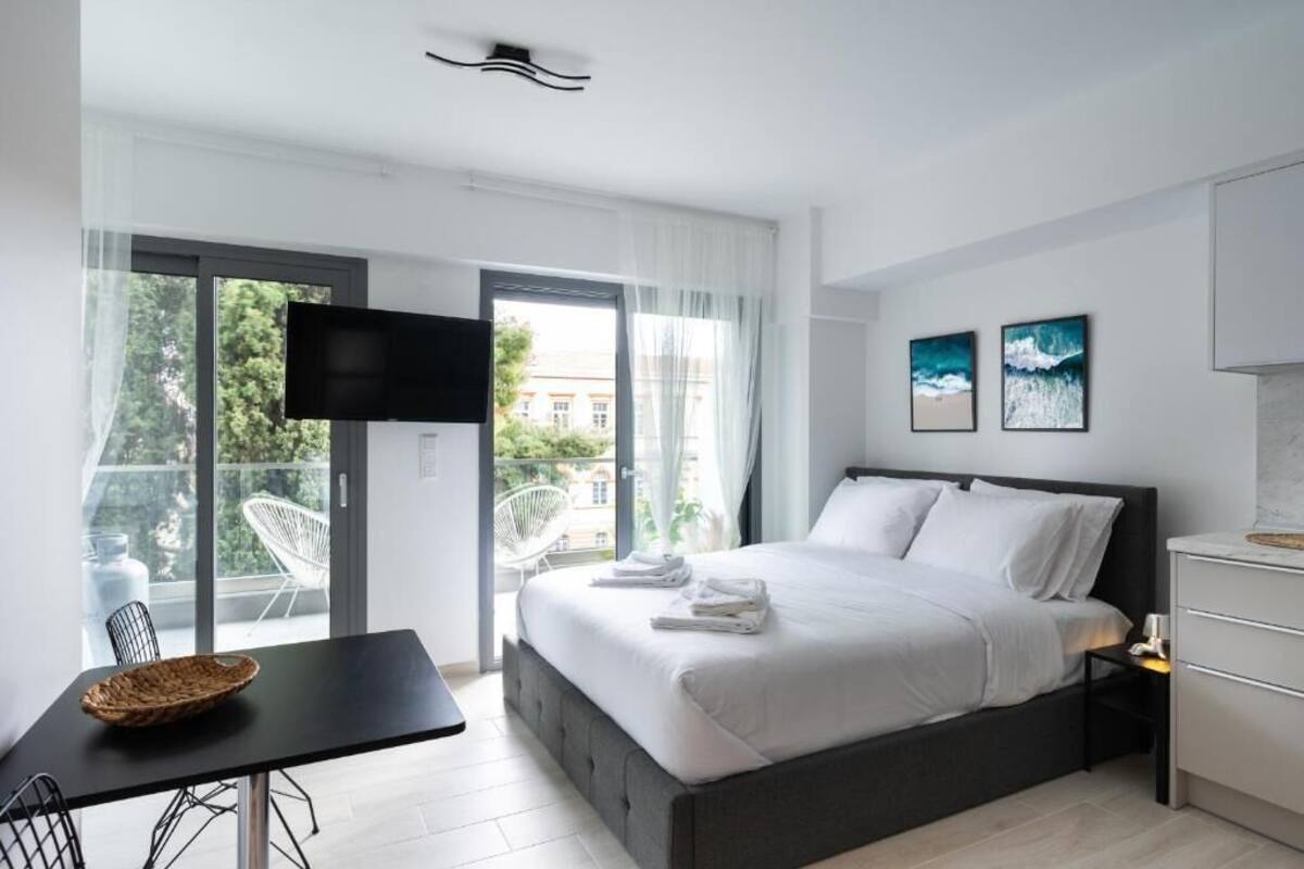 Een moderne hotelkamer met een bed, een televisie, een eettafel en een balkon met stoelen.