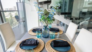 Ett matbord dukat med vävda bordsunderlägg, svarta servetter och blått glas, och en vas med blommor i mitten.