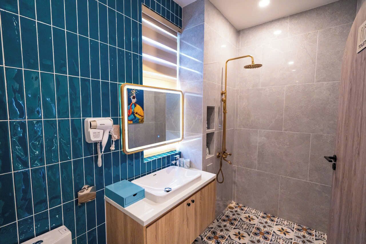 A modern bathroom with a blue-tiled wall, a white sink, a mirror with a gold frame, and a shower area.