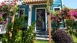 Una casa de dos pisos con fachada azul, una pérgola de madera y un jardín bien cuidado con flores rosas y arbustos.