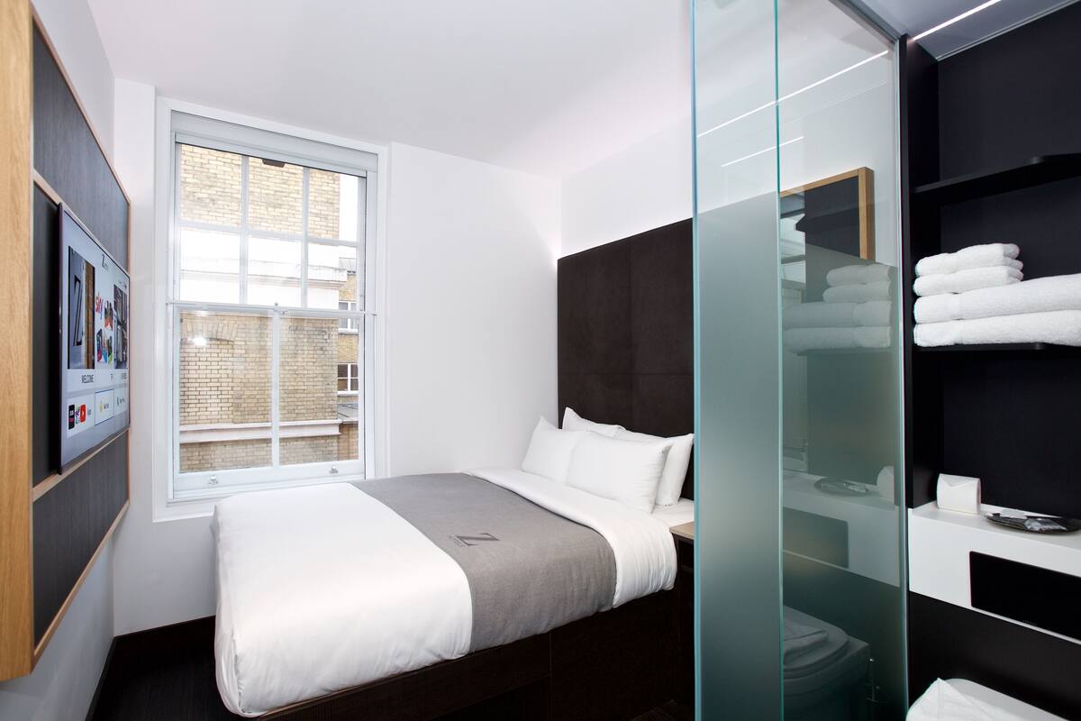Una habitación de hotel moderna con una cama grande, un separador de vidrio y vistas a la ciudad.