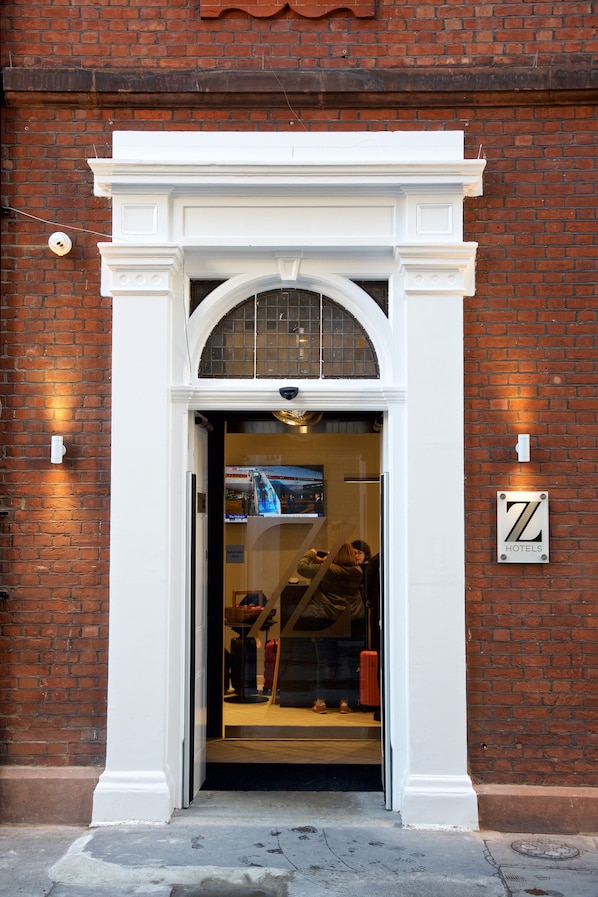 L’entrée d’un hôtel, avec une arche blanche, une enseigne bien visible portant le nom de l’hôtel et un mur en briques.