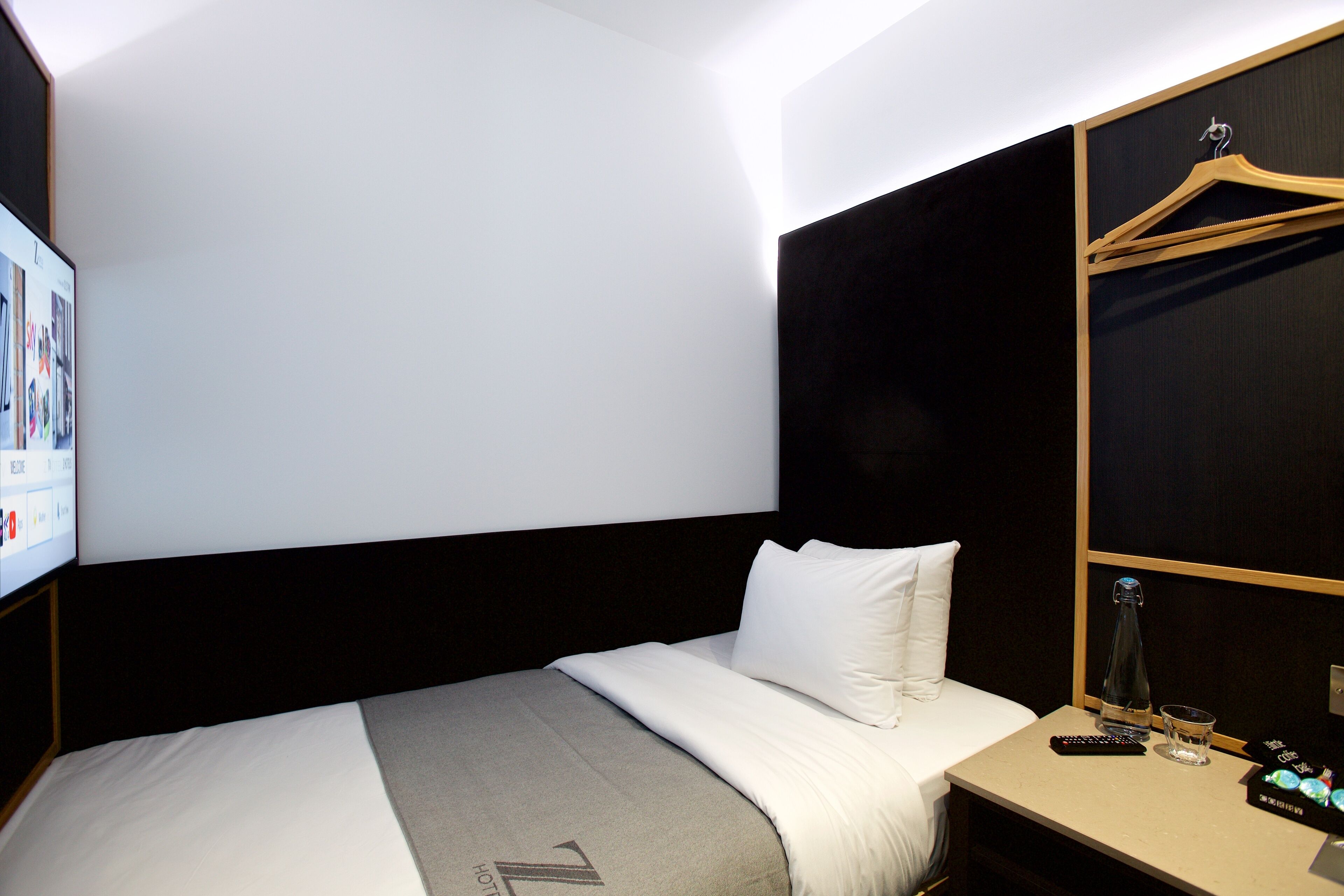Ein Hotelzimmer mit Bett, Nachttisch, Fernseher und Kleiderhaken.