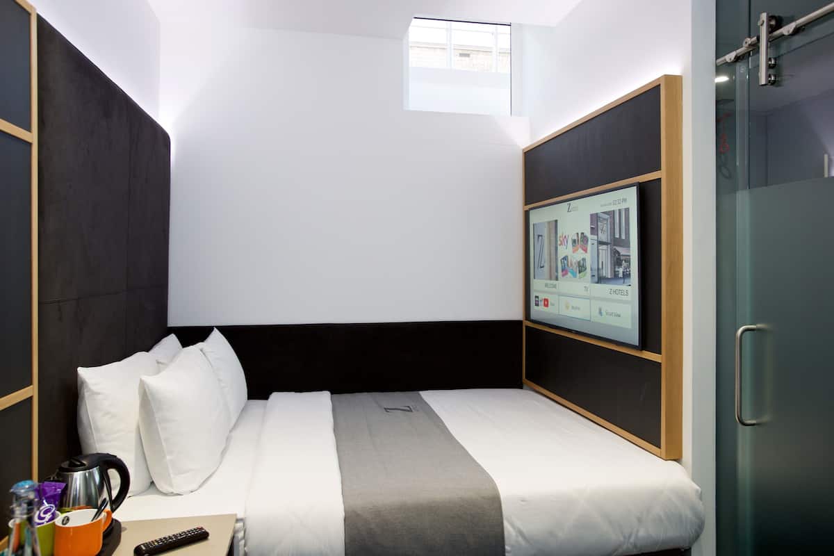 Una habitación de hotel moderna con una cama, un televisor montado en la pared, una ventana y una puerta.
