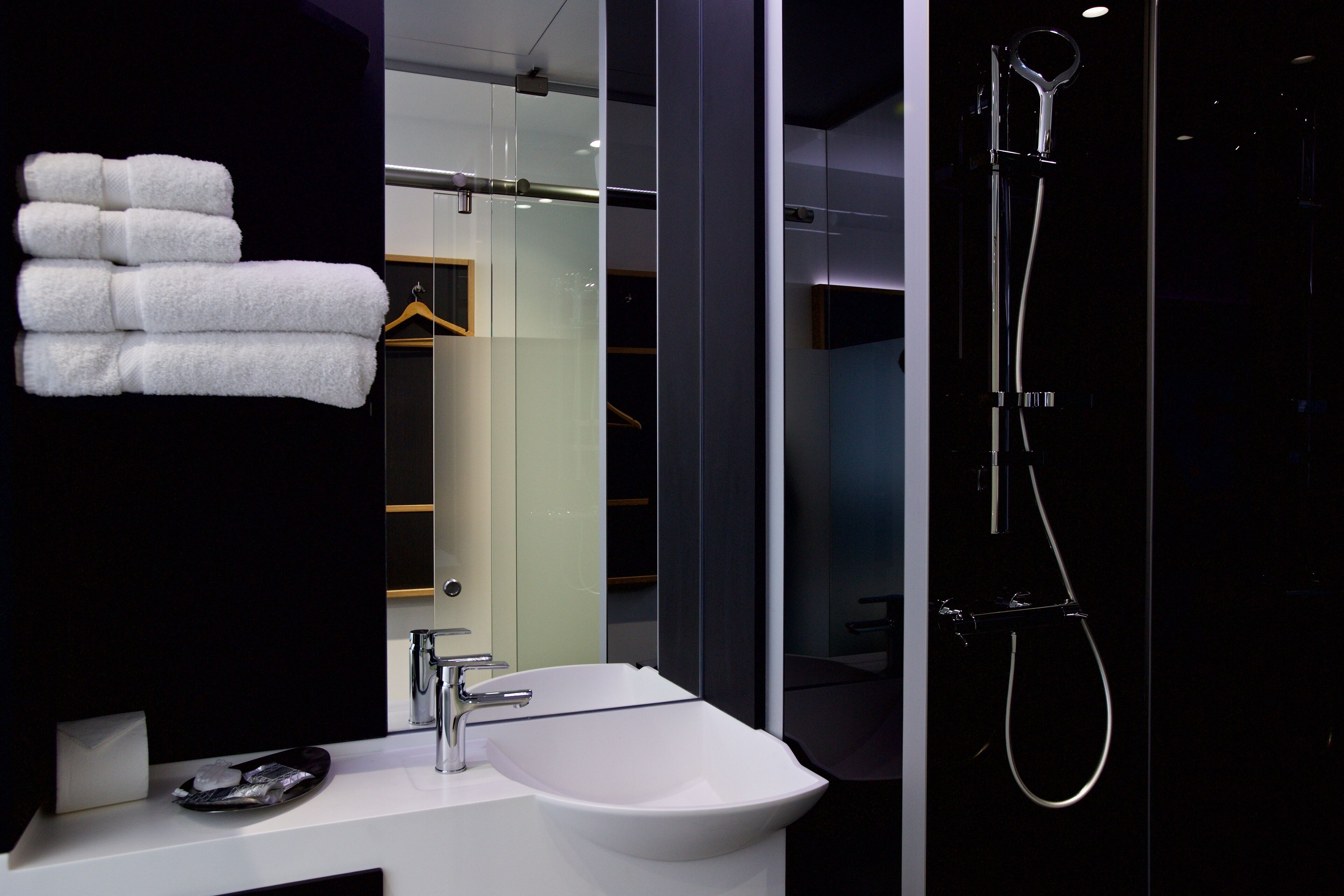 A modern bathroom with a white sink, a glass shower enclosure, and a towel rack with folded towels.